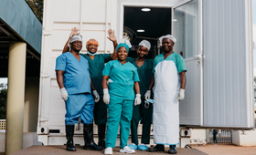 Equipa cirúrgica no exterior de uma clínica móvel, após uma cirurgia bem sucedida.